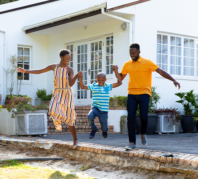 2 adults and a child jumping of the concrete onto grass