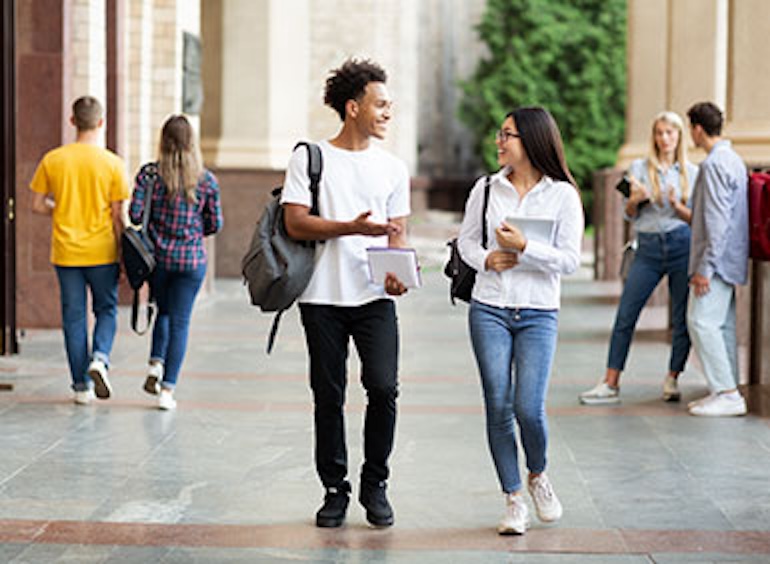 A college-aged male and female student wearing backpacks walking, talking, and smiling A college-aged male and female student wearing backpacks walking, talking, and smiling